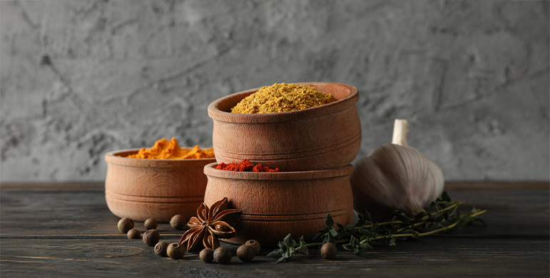 A close-up of Ayurvedic spices — turmeric, fennel, cumin, and coriander — arranged in wooden bowls.